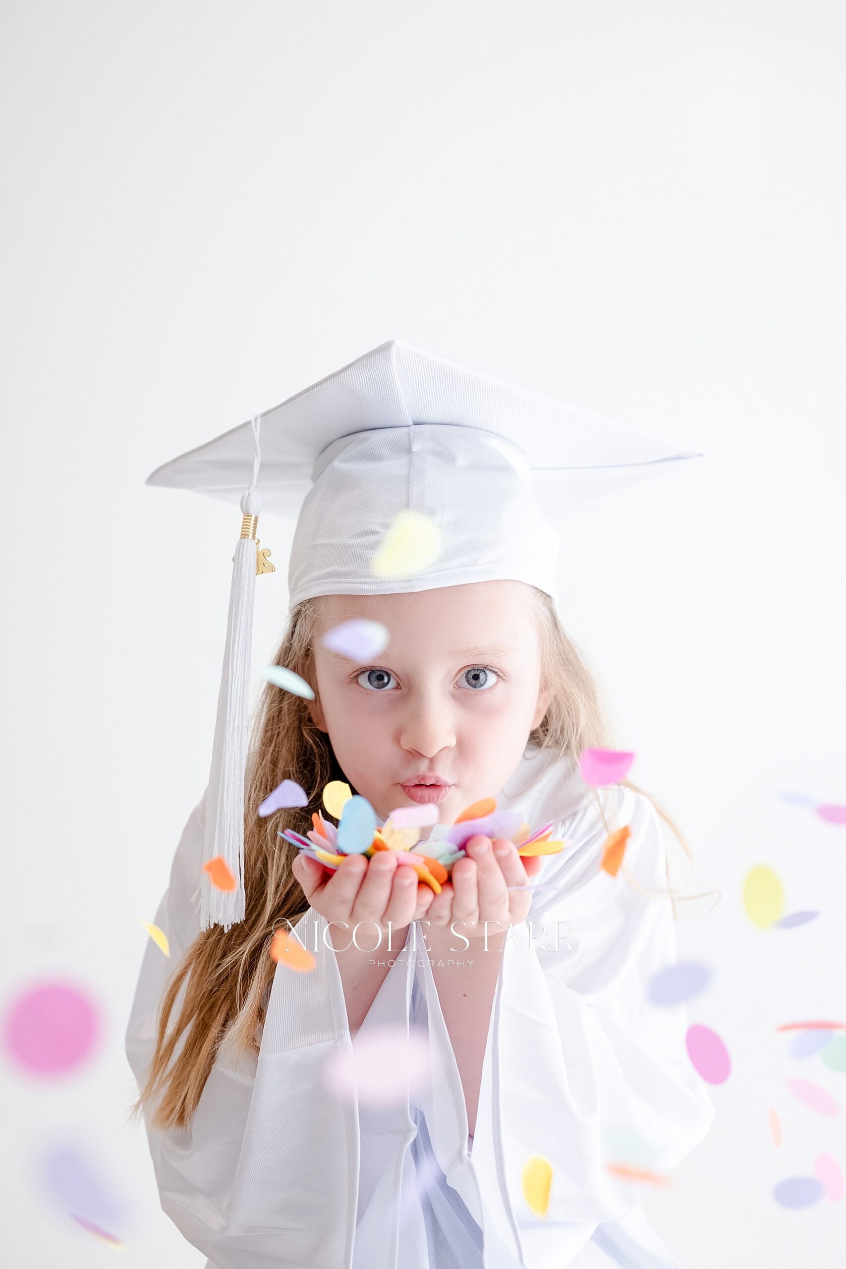 little girl blows confetti during celebratory tiny graduate session