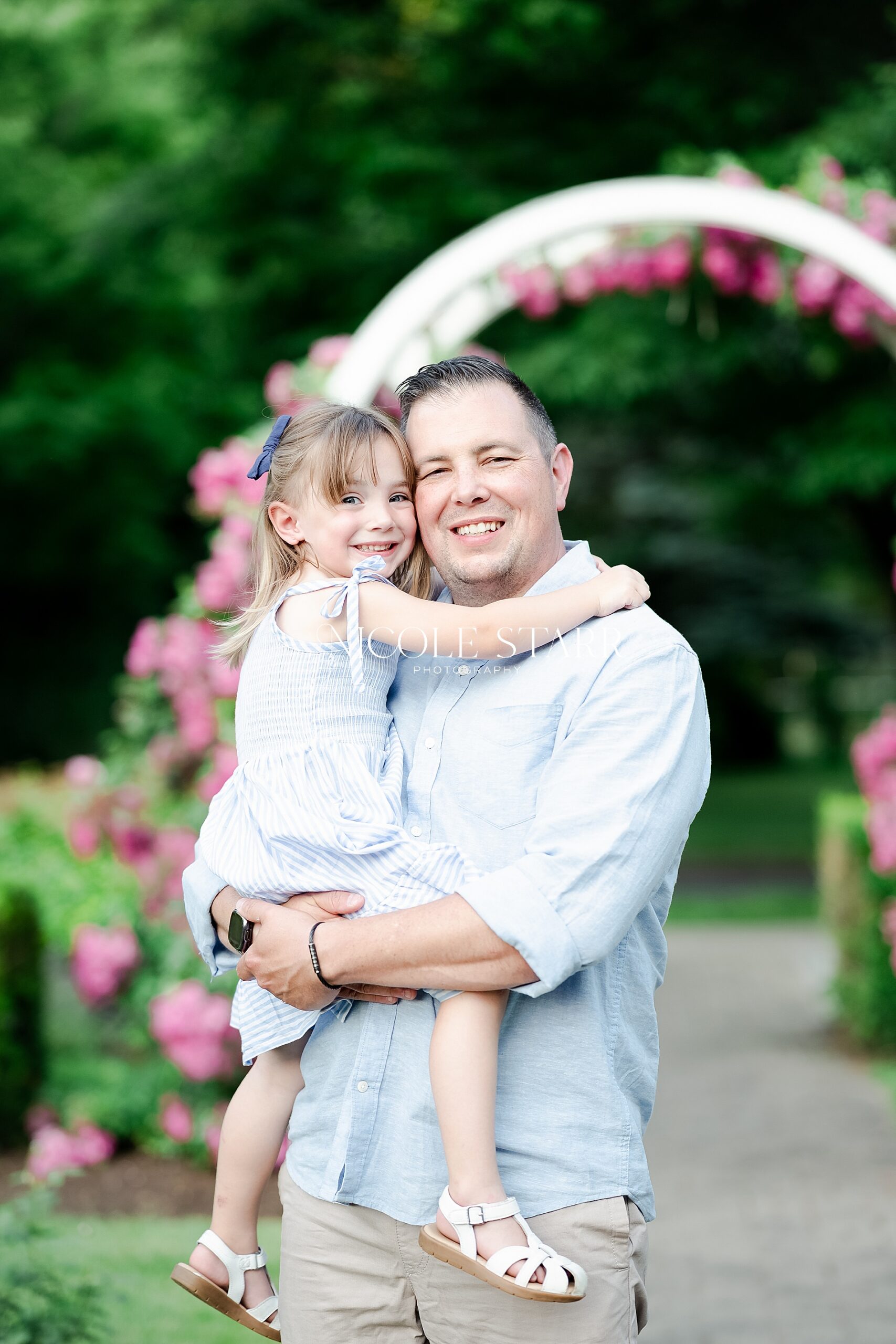ddad holds daughter in arms during Sun-Soaked Family Portraits in the Rose Garden