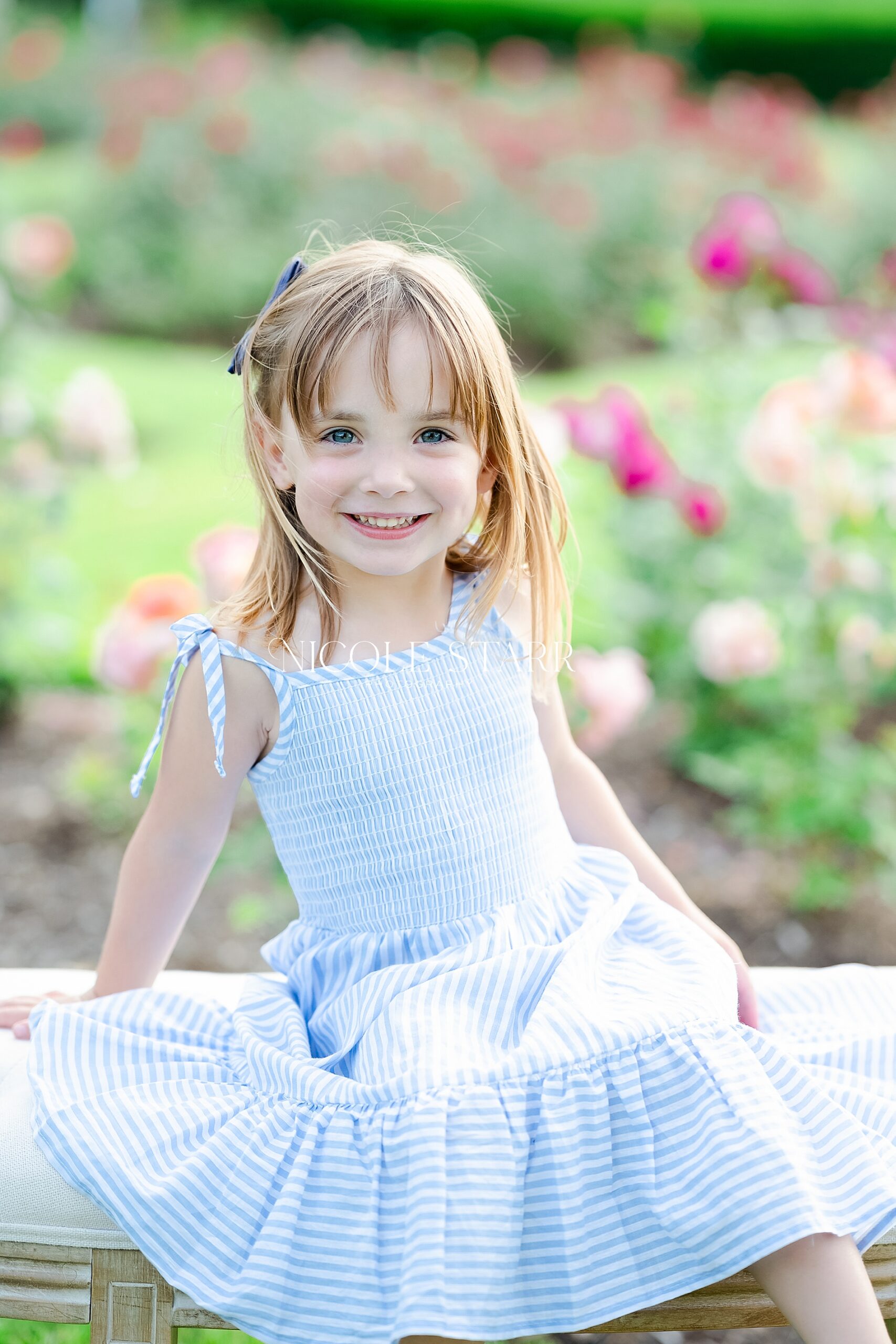 little girl in dress sits in rose garden