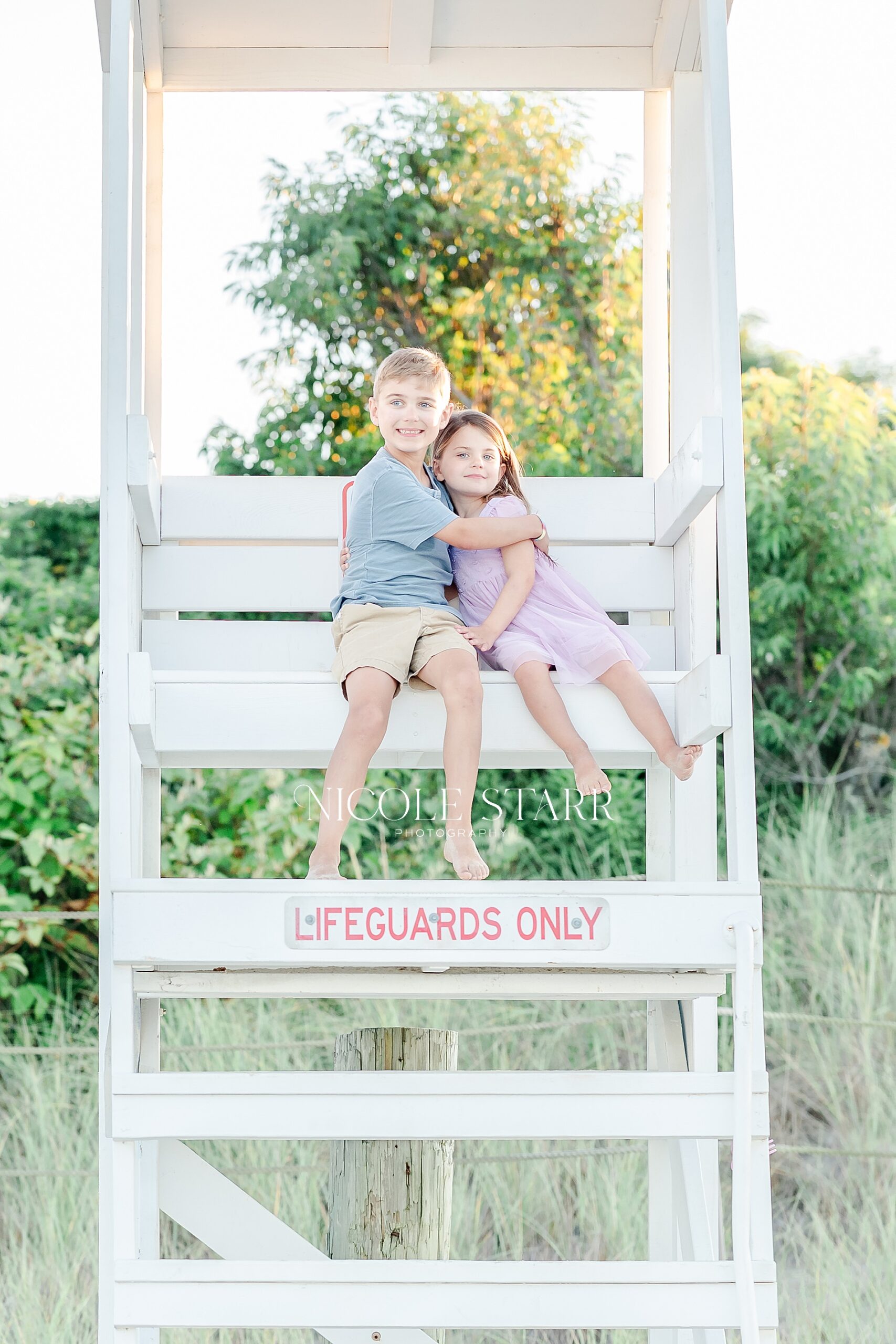 siblings sit together in white lifeguard stand